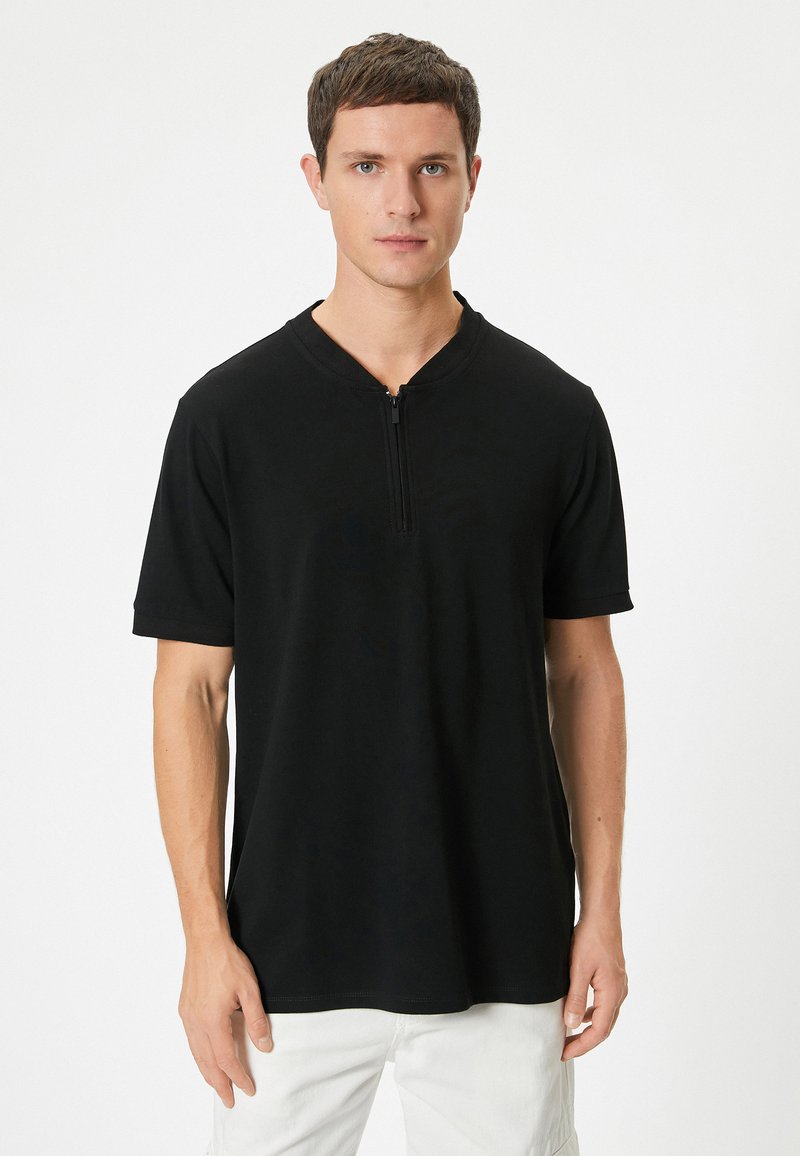 Sort kortærmet T-shirt med halv lynlås ved kraven. Lavet af glat stof, med en afslappet pasform og subtile sømdetaljer.