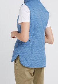 Gepolsterte hellblaue Weste mit hohem Kragen, Seitentaschen und abgerundetem Saum, aus weichem, leichtem Material gefertigt.