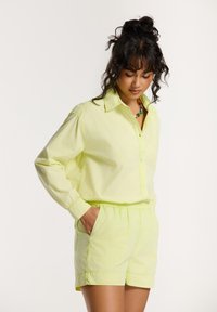 Lichtgele, knoopsluiting-shirt met lange mouwen, gecombineerd met bijpassende shorts. Beide zijn gemaakt van zachte stof met een elastische tailleband.