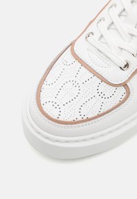 Witte geperforeerde leren sneaker met beige accenten, ronde neus, witte veters en een textuurzool. Beschikt over decoratieve stiksels.