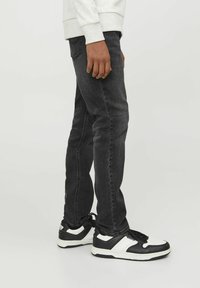 Jeans negros de corte ajustado con un acabado desgastado, diseño de cinco bolsillos y ligero estiramiento. Combinados con zapatillas deportivas en negro y blanco.