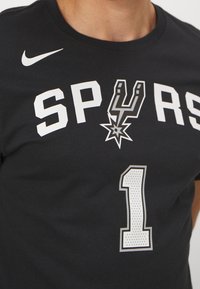 Schwarzes Baumwoll-T-Shirt mit "SPURS"-Logo in Weiß, mit einem silbernen Stern-Design über dem "S". Die Nummer "1" im durchbrochenen Stil darunter.