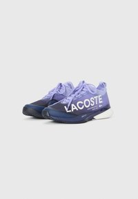 Lilla snøresko til trening med nett-overdel, med "LACOSTE"-merke i hvitt, en mørkeblå såle og teksturerte detaljer.