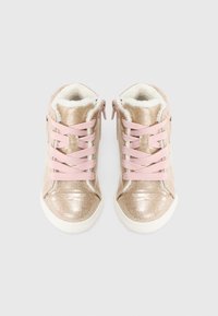 Παιδικά λαμπερά χρυσά αθλητικά παπούτσια με ροζ κορδόνια, λευκές σόλες και απαλό λευκό μάλλινο επένδυση, εμφανιζόμενα από πάνω σε λευκό φόντο.