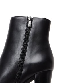 Bottine en cuir noir avec fermeture éclair sur le côté, quincaillerie en argent, texture lisse et talon épais.