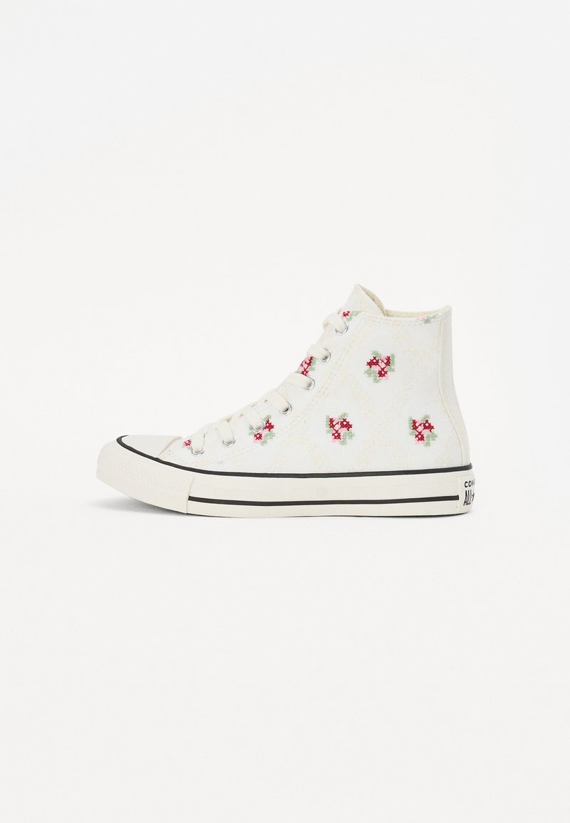 Hvite høye sneakers laget av lerret, med blomsterbroderi i rødt og grønt, samt en svart gummisåle og tåhette.
