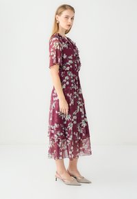 Pruimen bloemdress gemaakt van luchtige stof, met ruches, korte mouwen en een gelaagde rok. Gepaard met transparante hakken.