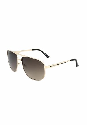 Occhiali da sole aviator in metallo dorato con lenti scure sfumate e terminali neri, con marchio GUESS sulle aste.
