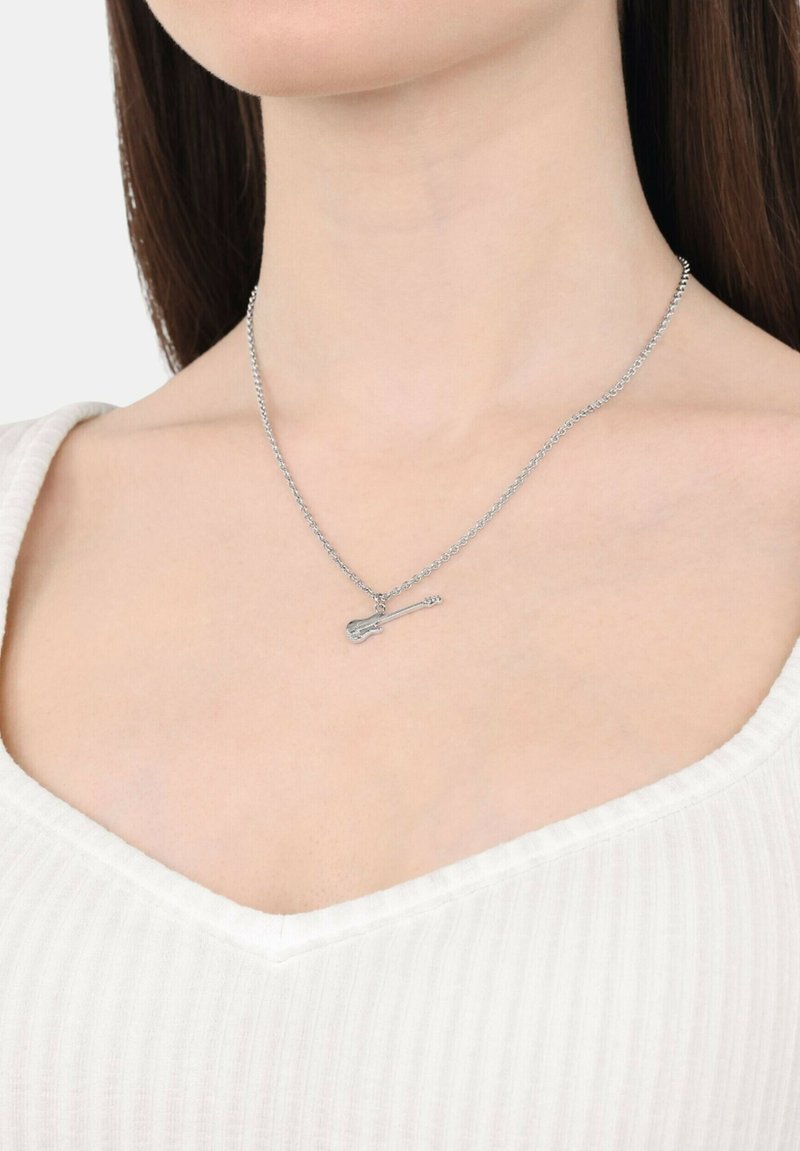 Collana d'argento con pendente a forma di chitarra, caratterizzata da una catena sottile e una texture liscia, indossata sopra un indumento bianco a scollo a V.
