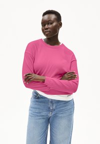 Rosa Langarm-Sweatshirt mit Rundhalsausschnitt und gerippten Bündchen, kombiniert mit hellblauen Hochbund-Jeans. Glatte Stofftextur.