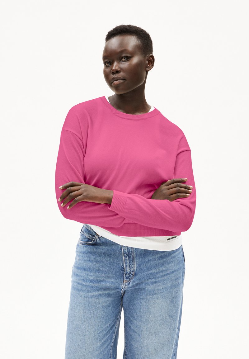 Rosa Langarm-Sweatshirt mit Rundhalsausschnitt und gerippten Bündchen, kombiniert mit hellblauen Hochbund-Jeans. Glatte Stofftextur.