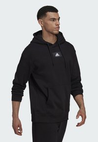 Sudadera con capucha negra fabricada en tejido suave, con un bolsillo frontal, puños acanalados y un logo de Adidas blanco en el pecho.