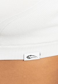 Witte textuurstof met een ribbelrand en een klein label met een zwart gestileerd dierenhoofdlogo op een lichtbruine achtergrond van huid.