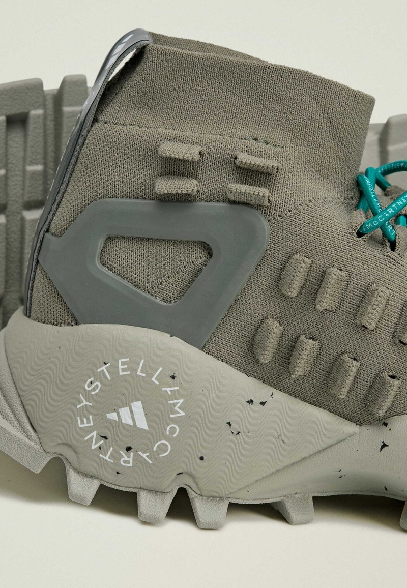 Grijze sportschoen met een gebreide bovenkant, rubberen hielsteun en een gestructurezool. Heeft turkooise veters en een logo op de loopzool.