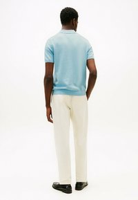 Polo de punto azul claro con mangas cortas, un dobladillo acanalado, combinado con pantalones color crema y zapatos negros, visto desde la parte de atrás.