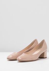 Beige lackläderpumps med rund tå och medelhög klack. Slät yta med en glansig finish.
