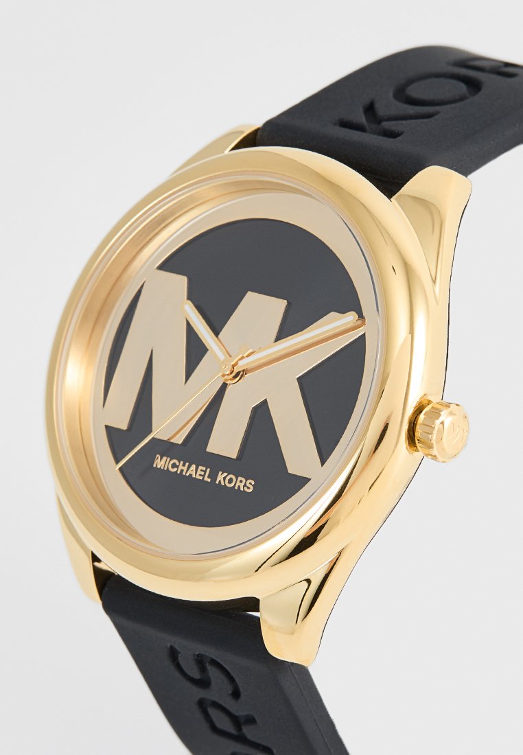 Reloj dorado con esfera negra que presenta un gran logo "MK" y el texto "Michael Kors". Correa de silicona negra con el nombre de la marca en relieve.