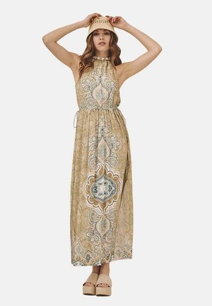 Vestido maxi en tonos tierras con intrincados patrones florales y de cachemira. Cuenta con una cintura elástica y un escote halter. Combinado con zapatos de plataforma de madera.