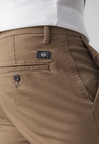Pantalon en coton marron avec une finition texturée, doté d'une poche arrière avec une étiquette marine et d'une fermeture à bouton marron.