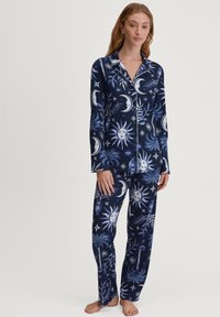 Navyblauw pyjama set met hemelse patronen van zonnen, manen en sterren in wit en lichtblauw, gemaakt van zachte stof met lange mouwen en broek.