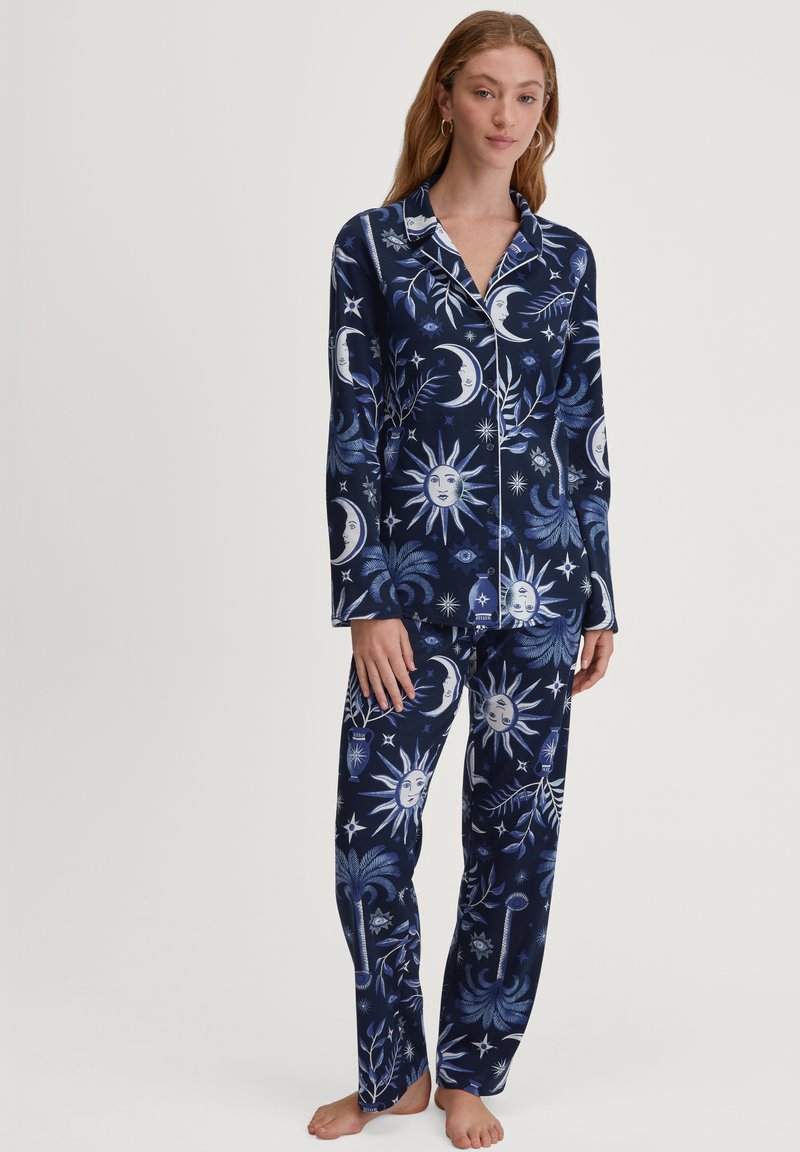 Navyblauw pyjama set met hemelse patronen van zonnen, manen en sterren in wit en lichtblauw, gemaakt van zachte stof met lange mouwen en broek.