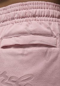 Primer plano de unos pantalones cortos de rizo rosa con cintura elástica y un bolsillo trasero plano.