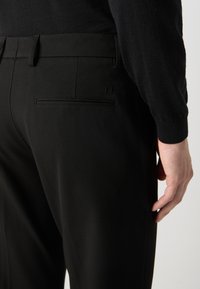 Pantalon noir ajusté en tissu lisse, slim fit, avec une poche arrière au design horizontal discret.