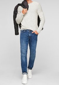 Light gray textured sweater, blue jeans, and white sneakers. Black jacket draped over shoulder. Casual outfit with simple design.