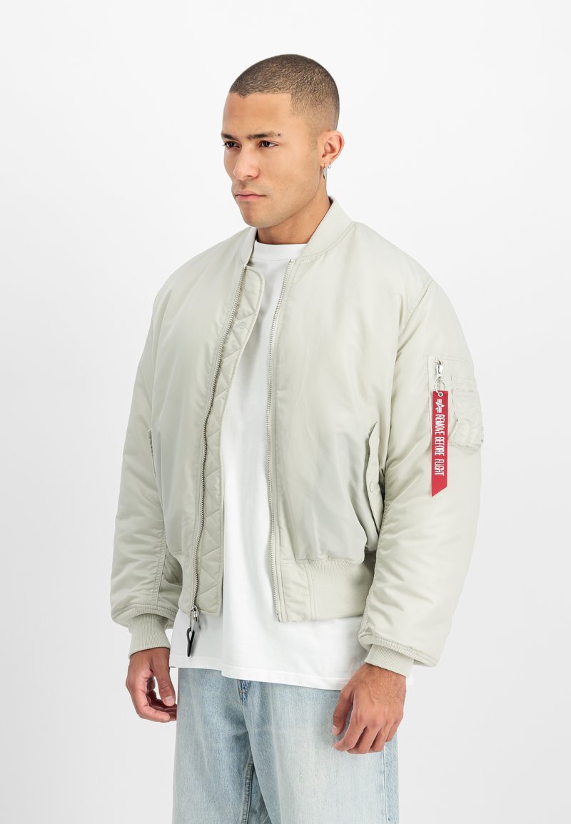 Világosszürke bomberdzseki cipzárral az elején, bordázott mandzsettákkal és piros címkével a bal ujján. Simább tapintású, rövidített szabású, minimalista stílusú.