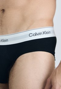 Schwarze Baumwollunterhosen mit einem elastischen Bund in Weiß und Grau, der das "Calvin Klein"-Logo trägt. Glatte Textur mit einer passenden Passform.