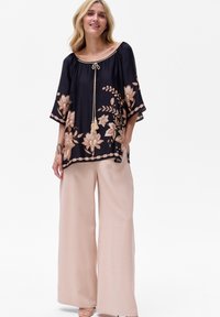 Granatowa bluzka z kwiecistym haftem w odcieniach brzoskwini i beżu, z krótkimi rękawami i dekoltem ze sznurkiem. Połączona z jasnymi spodniami.