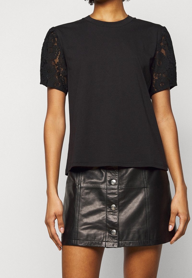 Camiseta negra con mangas de encaje, con cuello redondo y un corte relajado. Combinada con una minifalda negra de cuero con botones delanteros.