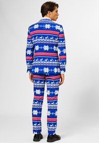 Traje azul con un patrón de copos de nieve y renos; incluye rayas rojas y blancas. Presenta un diseño a medida, bolsillos visibles y zapatos negros.
