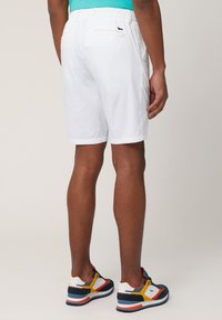 White shorts with an elastic waistband, featuring back pocket detailing. Paired with colorful athletic shoes and a turquoise shirt.