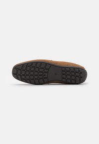 Brown suede shoe with a textured black rubber sole featuring a grid pattern for traction. Overall shape is streamlined and minimalistic.
