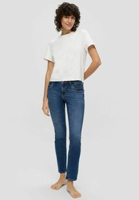 Witte, kortgegolfde, cropped t-shirt gecombineerd met strakke, donkerblauwe denim jeans. De stof lijkt zacht en glad. Geen zichtbare patronen of accenten.