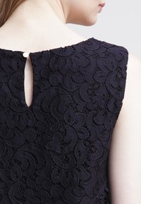 Navy lace dress featuring a floral pattern, rounded neckline, and a keyhole back closure with a small button detail.