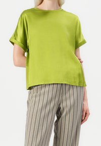 T-shirt en satin vert à manches courtes et col rond, associé à un pantalon clair à rayures. Le tissu a une texture lisse et brillante.