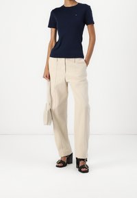 Navy short-sleeve t-shirt, beige tailored trousers, black heeled sandals with gold hardware, holding a beige handbag. Simple design and fit.