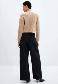 Maglione a trecce tagliato in morbido rosa cipria con maniche lunghe, abbinato a jeans neri a gamba larga. Tessuto dalla texture liscia e vestibilità rilassata.
