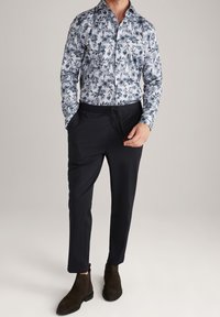 Koszula w kwiaty z długim rękawem w białych i niebieskich odcieniach, zestawiona z czarnymi spodniami na sznurki. Brązowe zamszowe botki za kostkę dopełniają stylizację.