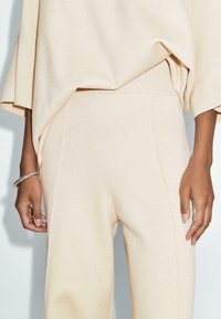 Beżowy sweter i pasujące szerokie spodnie z miękkiego, teksturowanego materiału. Sweter ma luźny krój z prążkowanym wykończeniem u dołu, spodnie posiadają boczne szwy.