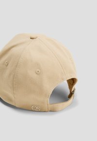 Casquette de baseball en coton beige avec une visière incurvée, une sangle ajustable et un logo "QS" brodé. Tissu texturé et détails de couture visibles.