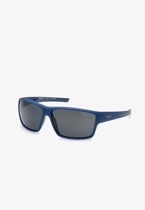 Gafas de sol de plástico azul con lentes grises. Forma rectangular, montura ancha, textura suave y diseño sin costuras. Marca pequeña en el costado.