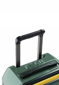 Valigia rigida di colore verde scuro con superficie texturizzata, manico telescopico nero, zip gialla e "Delsey Paris" inciso sulla parte superiore.