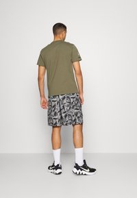 Olive zelené tričko, krátké rukávy; vzorované černobílé šortky s abstraktními tvary; černé tenisky s bílými detaily; kotníkové ponožky.