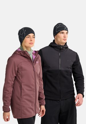Zwei Erwachsene in Winterjacken und schwarzen Mützen stehen nebeneinander und schauen leicht nach rechts.