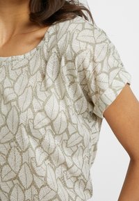 Lichtgroen top met een bladerenpatroon, ronde halslijn en korte mouwen. Het materiaal lijkt lichtgewicht met een zachte textuur.