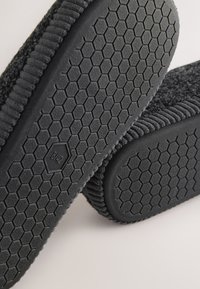 Črni čevlji brez vezalk z zgornjim delom iz teksturirane tkanine in gumijastim podplatom s šestkotnim vzorcem ter vtisnjenim napisom s številko velikosti.