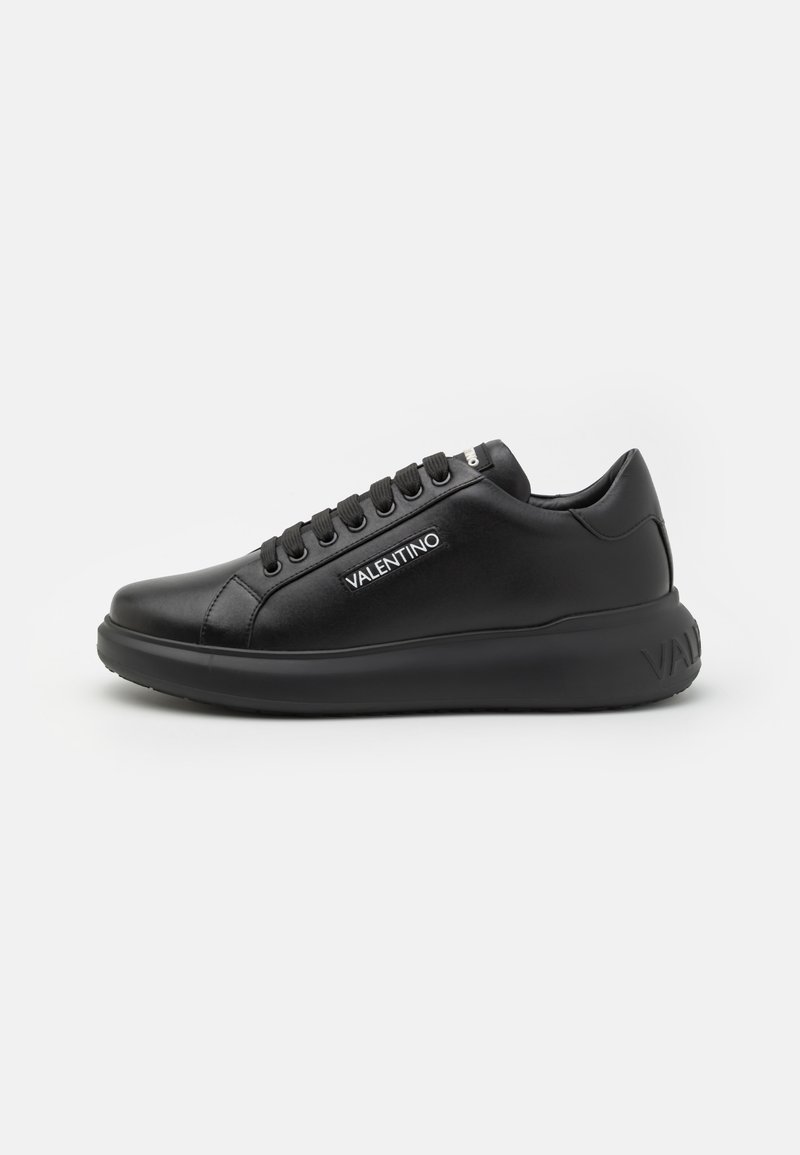 Black leather sneaker with a smooth finish, lace-up design, round toe, padded collar, and a thick sole featuring a logo at the heel.